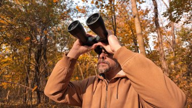 Kuşları ve diğer hayvanları dürbünle gözlemleyen amatör kuş gözlemcisi..