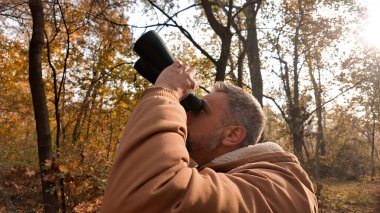 Kuşları ve diğer hayvanları dürbünle gözlemleyen amatör kuş gözlemcisi..