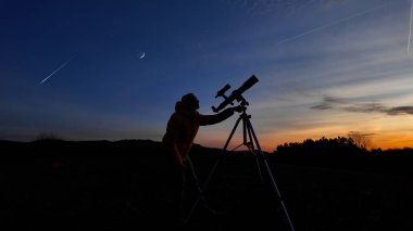 Amatör astronom akşam gökyüzüne bakıyor, gezegenleri, yıldızları, ayı ve teleskopla diğer gök cisimlerini gözlemliyor..