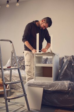 Yeni bir dairede çalışan ve mobilya montajlayan bir adam..