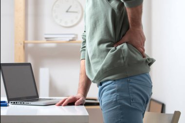 Dizüstü bilgisayarla uğraşırken sırt ağrısı çeken bir adam..