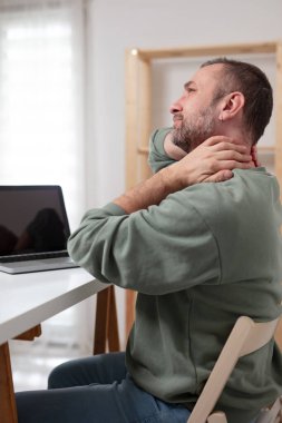 Dizüstü bilgisayarda çalışırken boynu ağrıyan bir adam..