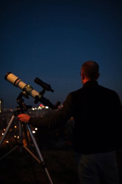 Amatör astronom akşam gökyüzüne bakıyor, gezegenleri, yıldızları, ayı ve diğer gök cisimlerini şehir merkezinde teleskopla inceliyor..