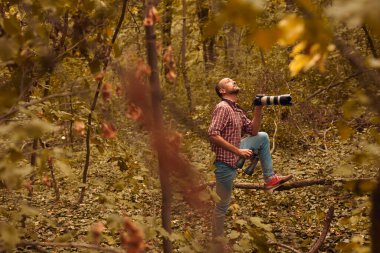Dürbün ve kamera kullanan adam doğada kuşları ve hayvanları izliyor..
