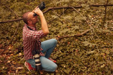 Dürbün ve kamera kullanan adam doğada kuşları ve hayvanları izliyor..