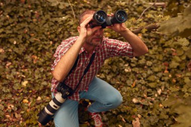 Dürbün ve kamera kullanan adam doğada kuşları ve hayvanları izliyor..