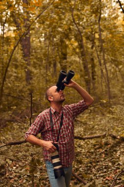 Dürbün ve kamera kullanan adam doğada kuşları ve hayvanları izliyor..