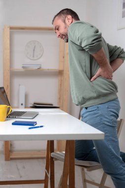 Dizüstü bilgisayarla uğraşırken sırt ağrısı çeken bir adam..