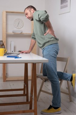 Dizüstü bilgisayarla uğraşırken sırt ağrısı çeken bir adam..