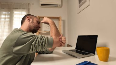 Dizüstü bilgisayarla uğraşırken dirsek ağrısı çeken bir adam..