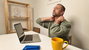 Dizüstü bilgisayarda çalışırken boynu ağrıyan bir adam..