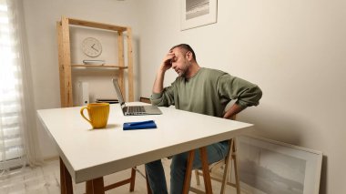 Dizüstü bilgisayarda çalışırken başı ağrıyan bir adam..