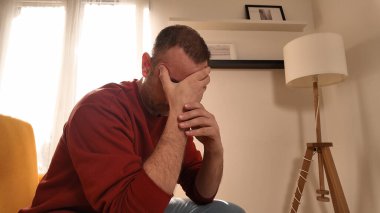 Başı ağrıyan adam evdeki kanepede oturuyor..