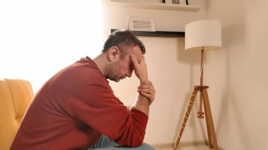 Başı ağrıyan adam evdeki kanepede oturuyor..