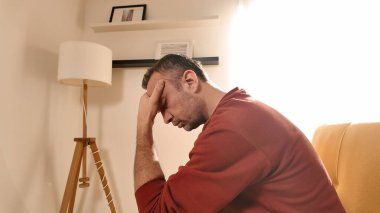 Başı ağrıyan adam evdeki kanepede oturuyor..