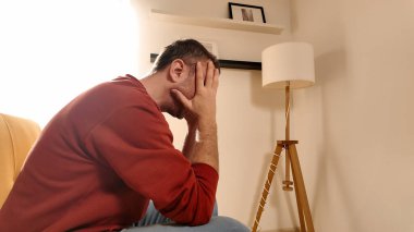 Başı ağrıyan adam evdeki kanepede oturuyor..