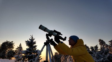 Amatör astronom kışın teleskopla gökyüzüne bakıyor..