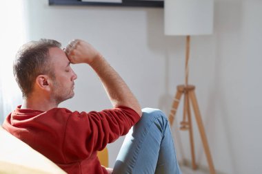 Başı ağrıyan adam evdeki kanepede oturuyor..