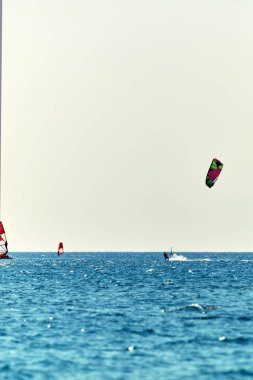 Rüzgâr sörfçüleri mavi deniz sularında eğleniyor.