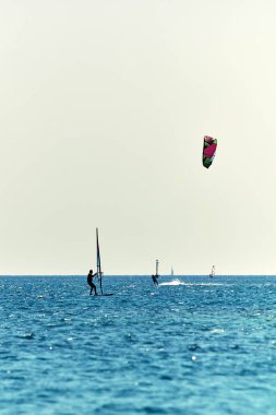 Rüzgâr sörfçüleri mavi deniz sularında eğleniyor.