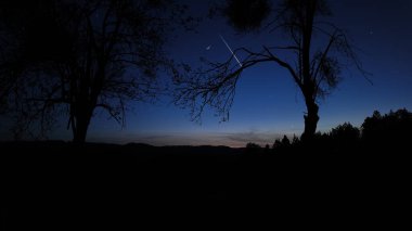 Countryside silhouettes under the stars, meteor trail and crescent Moon. clipart