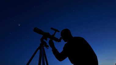 Amatör astronom akşam gökyüzüne bakıyor, gezegenleri, yıldızları, ayı ve teleskopla diğer gök cisimlerini gözlemliyor..