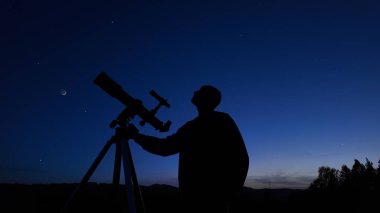 Amatör astronom akşam gökyüzüne bakıyor, gezegenleri, yıldızları, ayı ve teleskopla diğer gök cisimlerini gözlemliyor..