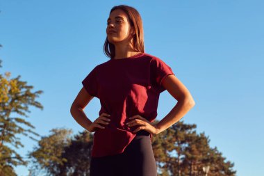 Genç bir kadın güneşli yaz gününde şehir parkında egzersiz ve koşu için ısınıyor..