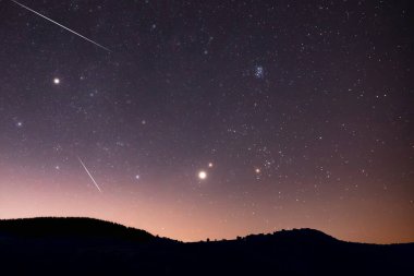 Samanyolu yıldızları, gezegenler, kuyruklu yıldızlar ve meteor yağmuru izleri ve kırsal ağaç siluetleri.