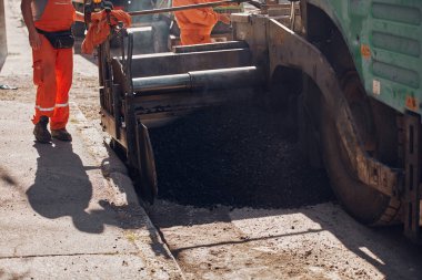 İnşaat işçileri kamu caddesinde yeni bir asfalt tabakası üzerinde çalışıyorlar..