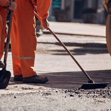 İnşaat işçileri kamu caddesinde yeni bir asfalt tabakası üzerinde çalışıyorlar..