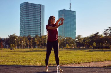 Egzersiz sonrası esneyen ve güneşli yaz gününde şehir parkında koşan genç bir kadın..