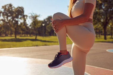 Egzersiz sonrası esneyen ve güneşli yaz gününde şehir parkında koşan genç bir kadın..