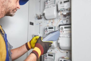 Technician reading consumption and charging on a wireless electricity power meter station in a building. clipart