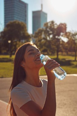 Şehir parkında koşudan ve egzersizden sonra su içen genç bir kadın.