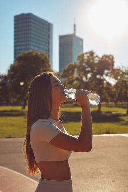Şehir parkında koşudan ve egzersizden sonra su içen genç bir kadın.