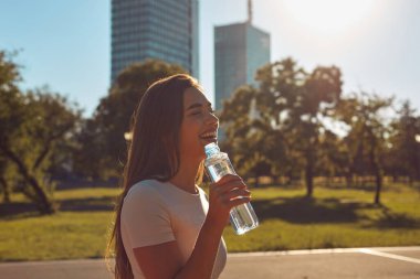 Şehir parkında koşudan ve egzersizden sonra su içen genç bir kadın.