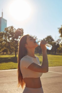 Şehir parkında koşudan ve egzersizden sonra su içen genç bir kadın.