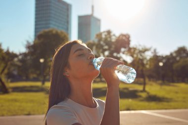 Şehir parkında koşudan ve egzersizden sonra su içen genç bir kadın.