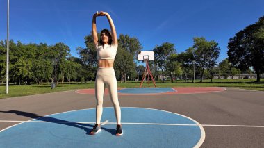 Egzersiz sonrası esneyen ve güneşli yaz gününde şehir parkında koşan genç bir kadın..