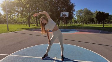 Egzersiz sonrası esneyen ve güneşli yaz gününde şehir parkında koşan genç bir kadın..