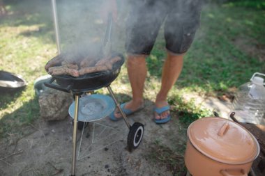 Man preparing barbeque in the garden on a hot summer day. clipart