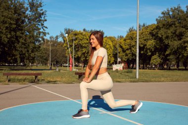 Egzersiz sonrası esneyen ve güneşli yaz gününde şehir parkında koşan genç bir kadın..