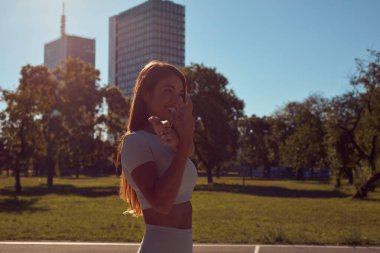 Egzersiz sonrası esneyen ve güneşli yaz gününde şehir parkında koşan genç bir kadın..