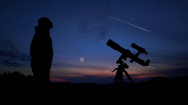 Amatör astronom akşam gökyüzüne bakıyor, gezegenleri, yıldızları, ayı ve teleskopla diğer gök cisimlerini gözlemliyor..