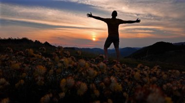 Kolları doğada açık bir adamın silueti..
