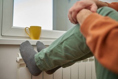 Soğuk bir kış gününde evin ısıtıcı kaloriferinde çoraplı bir adamın ayakları..