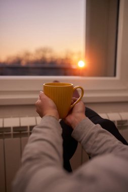 Soğuk bir kış gününde sıcak çay içen bir kadın, çoraplarını giymiş, radyatörünü ısıtıyor..