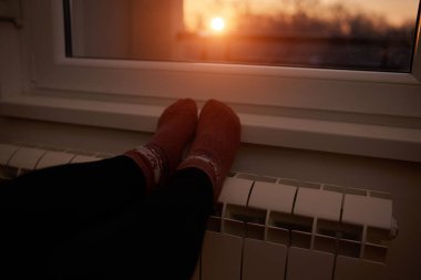 Soğuk bir kış gününde ev ısıtıcı radyatörde çoraplı bir kadının ayakları..