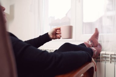 Soğuk bir kış gününde, sıcak çay içen bir kadın, çoraplarıyla evde ısıtma radyatöründe çoraplarını giyiyor..